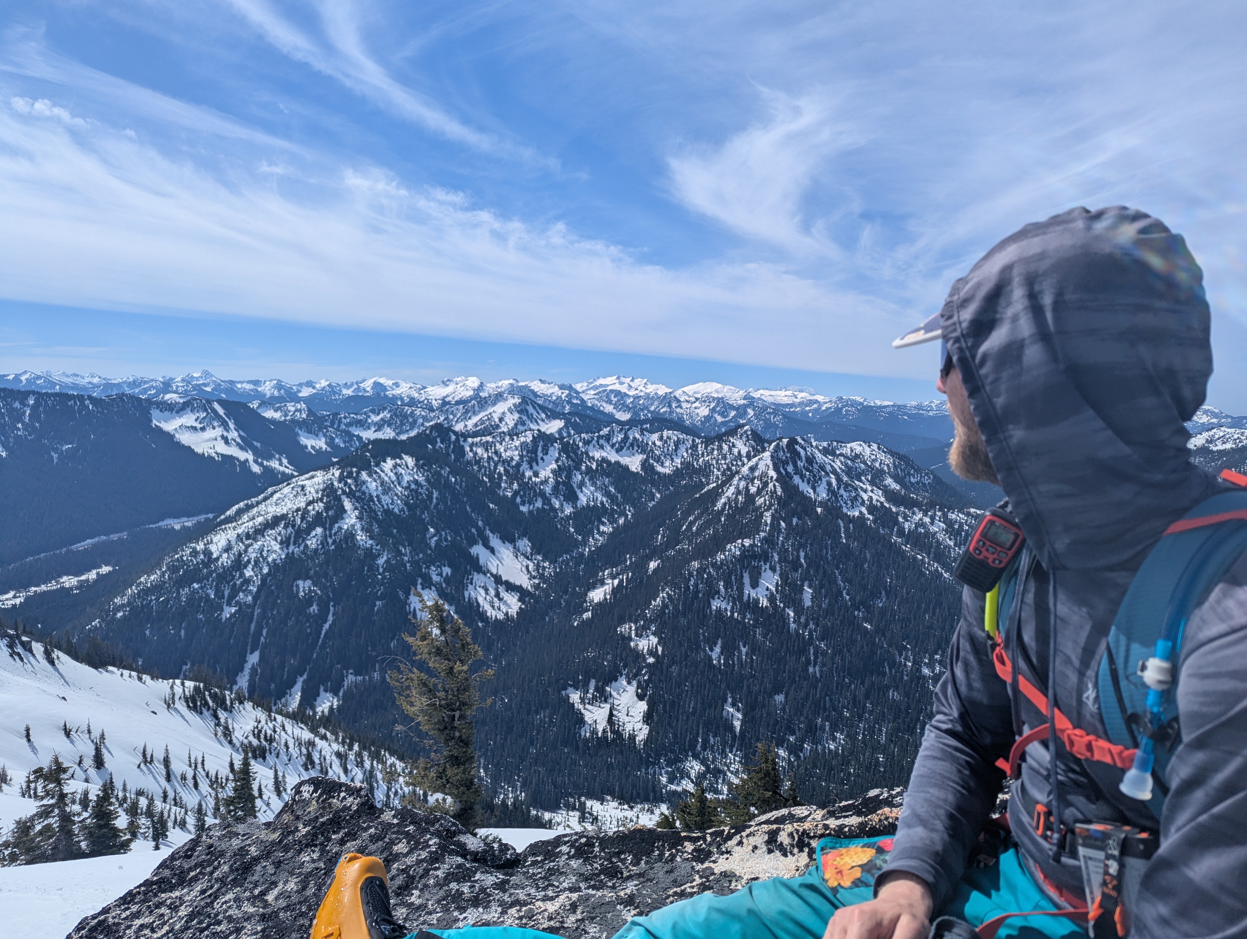 The same skier sitting on a summit looking out at the mountains