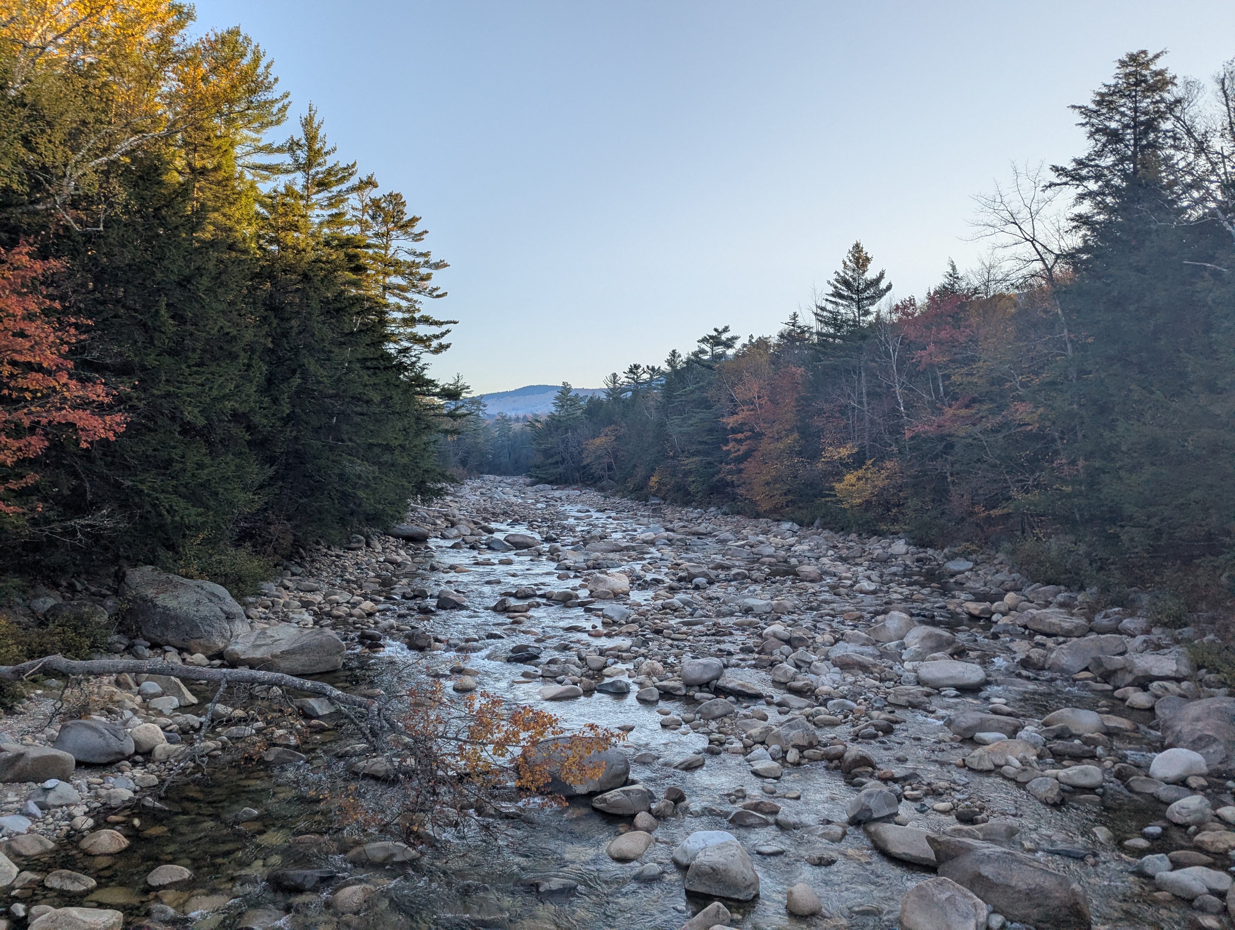 A low river with rocks strewn about, colorful leaves on the trees on either side