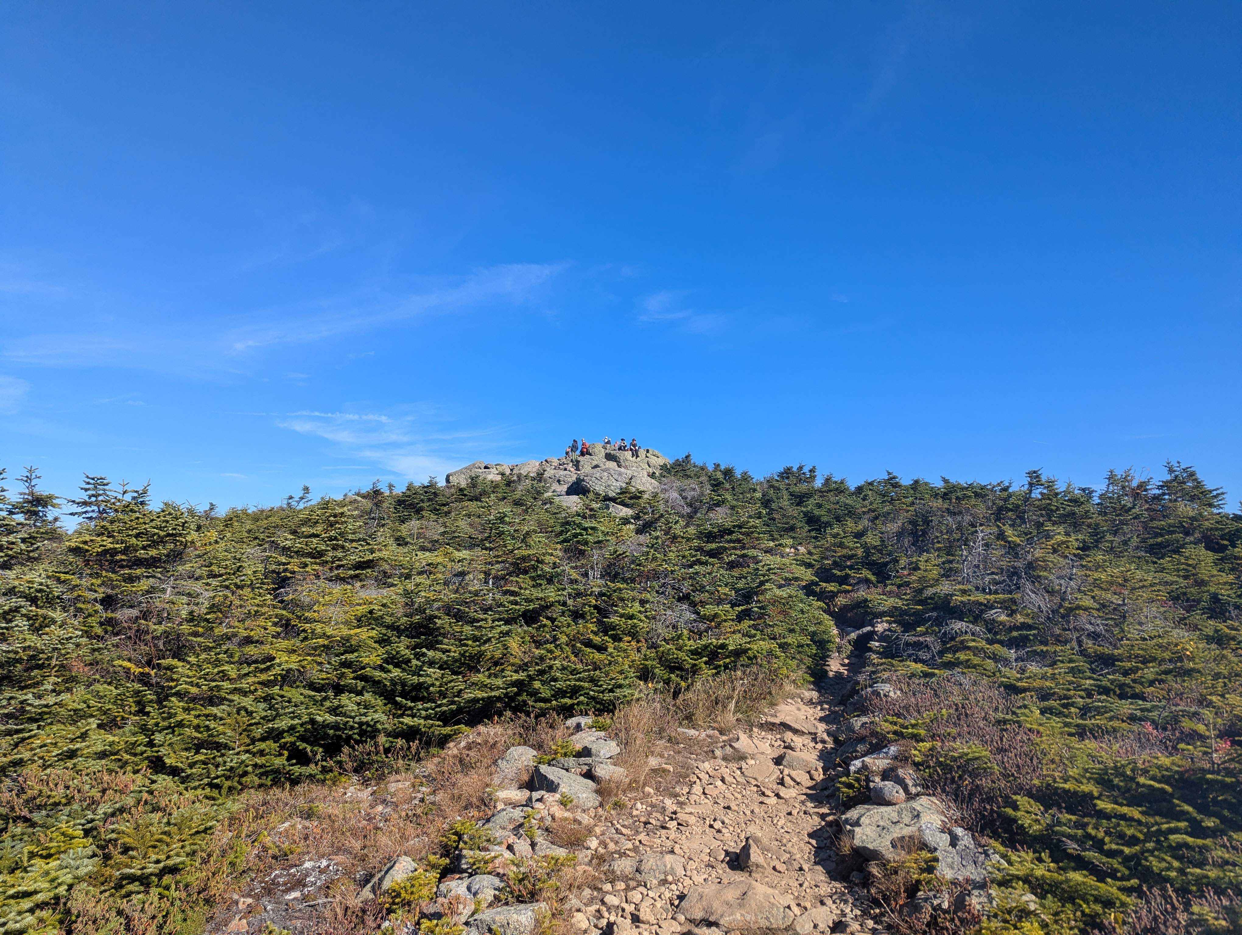 A rocky sub-summit with several people visible in the distance