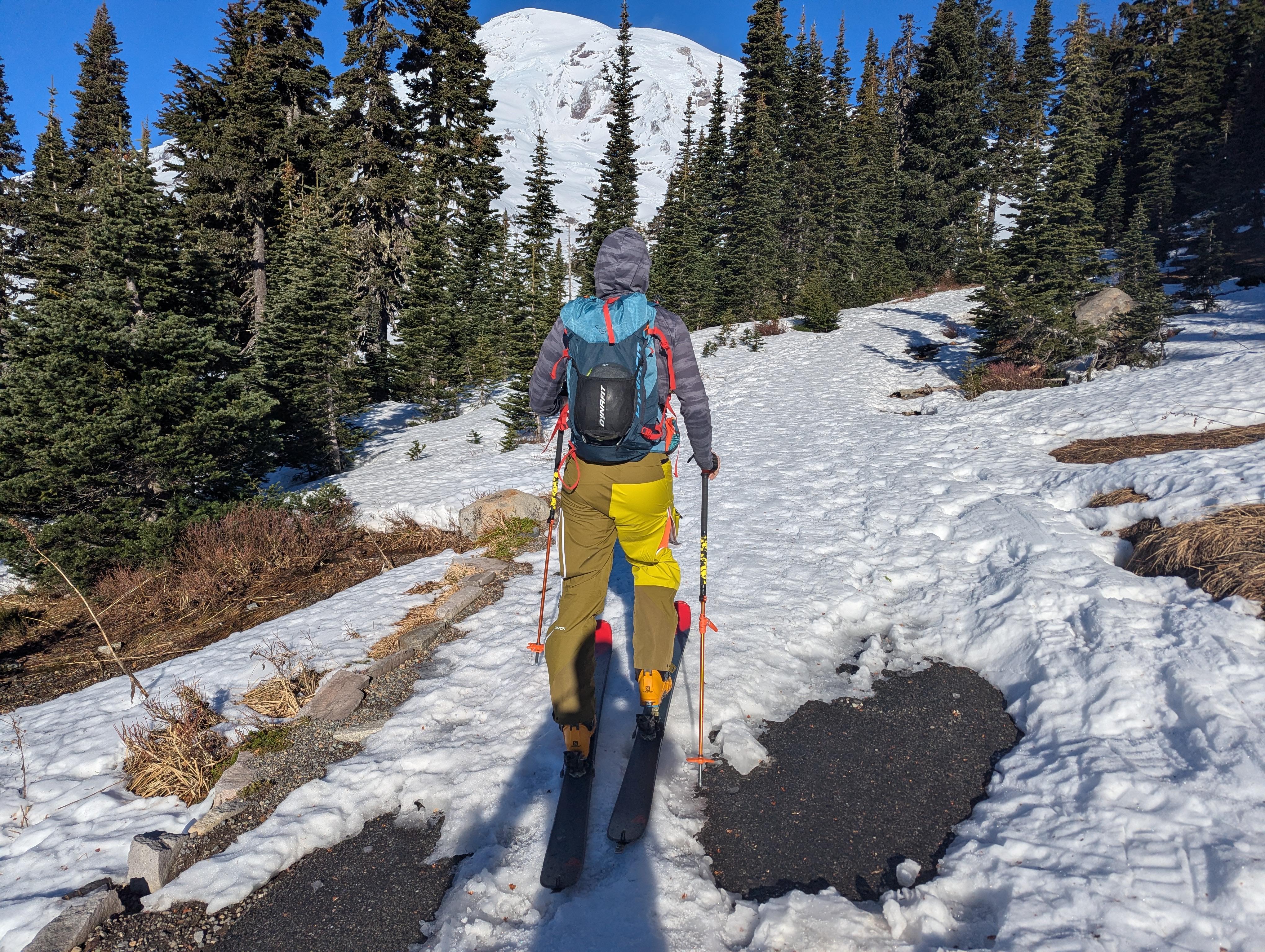 A skier touring on a narrow strip of snow between two exposed sections of paved trail