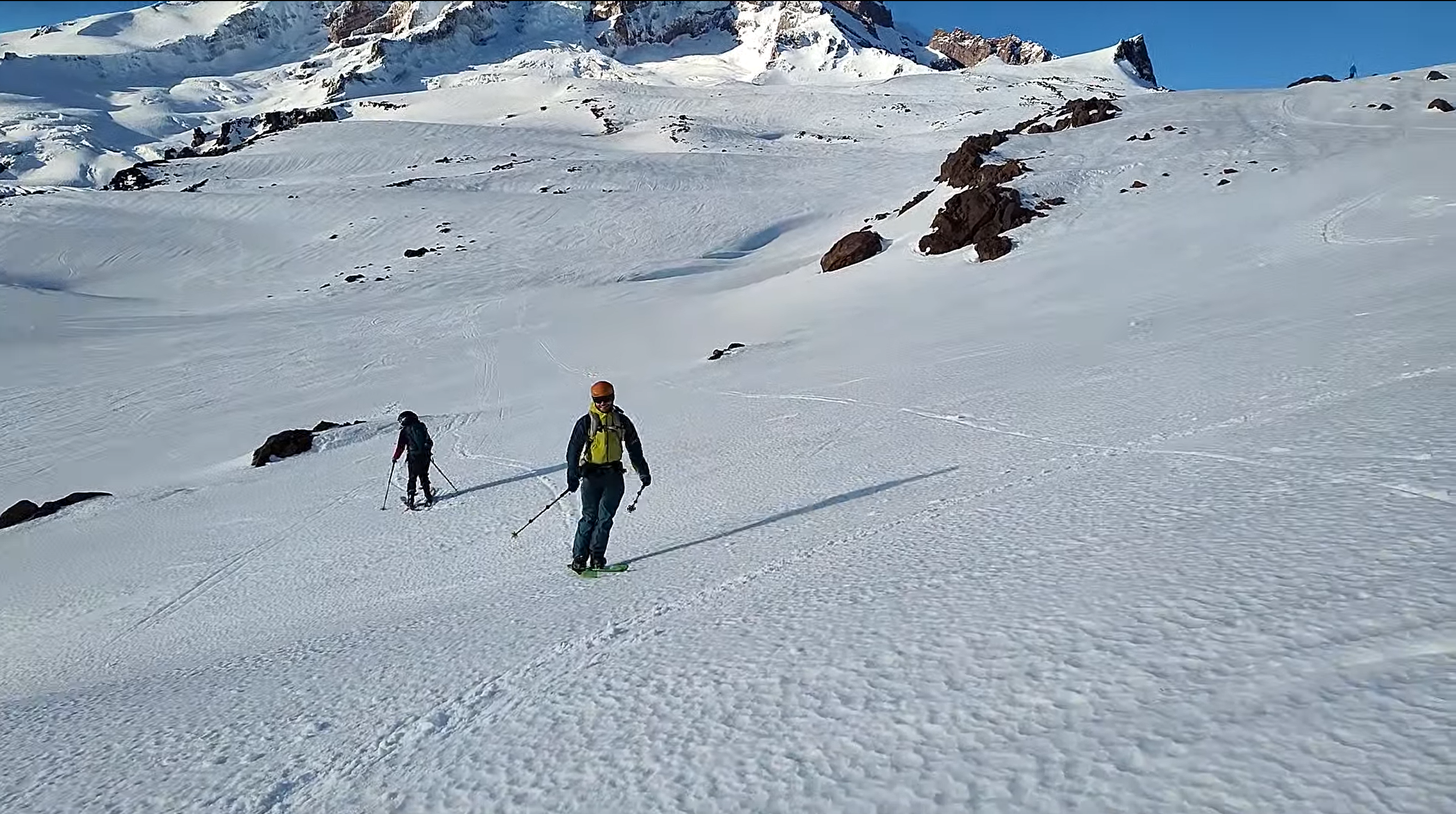 Two skiers on a slope, with a large mountain above